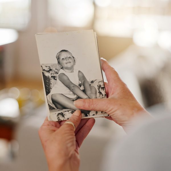 Hand, nostalgia and senior person with picture frame for mourning, loss or grief with history in house. Comfort, memory and elderly patient with photo for reflection or remembrance in retirement home.